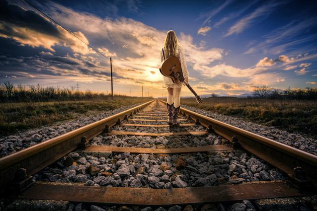 une femme marchant sur les rails, guitare à la main